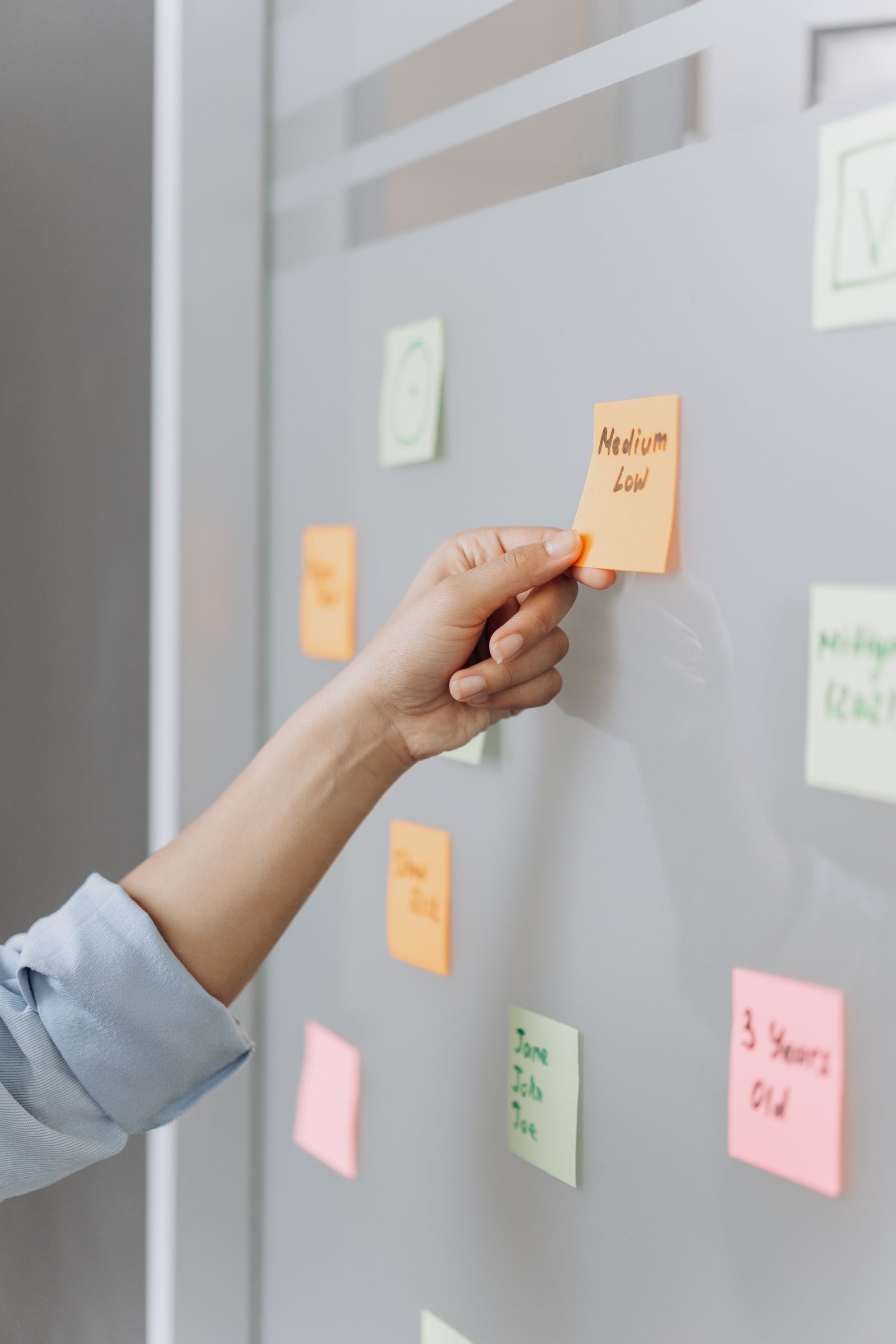A hand placing a sticky note on a glass wall of notes