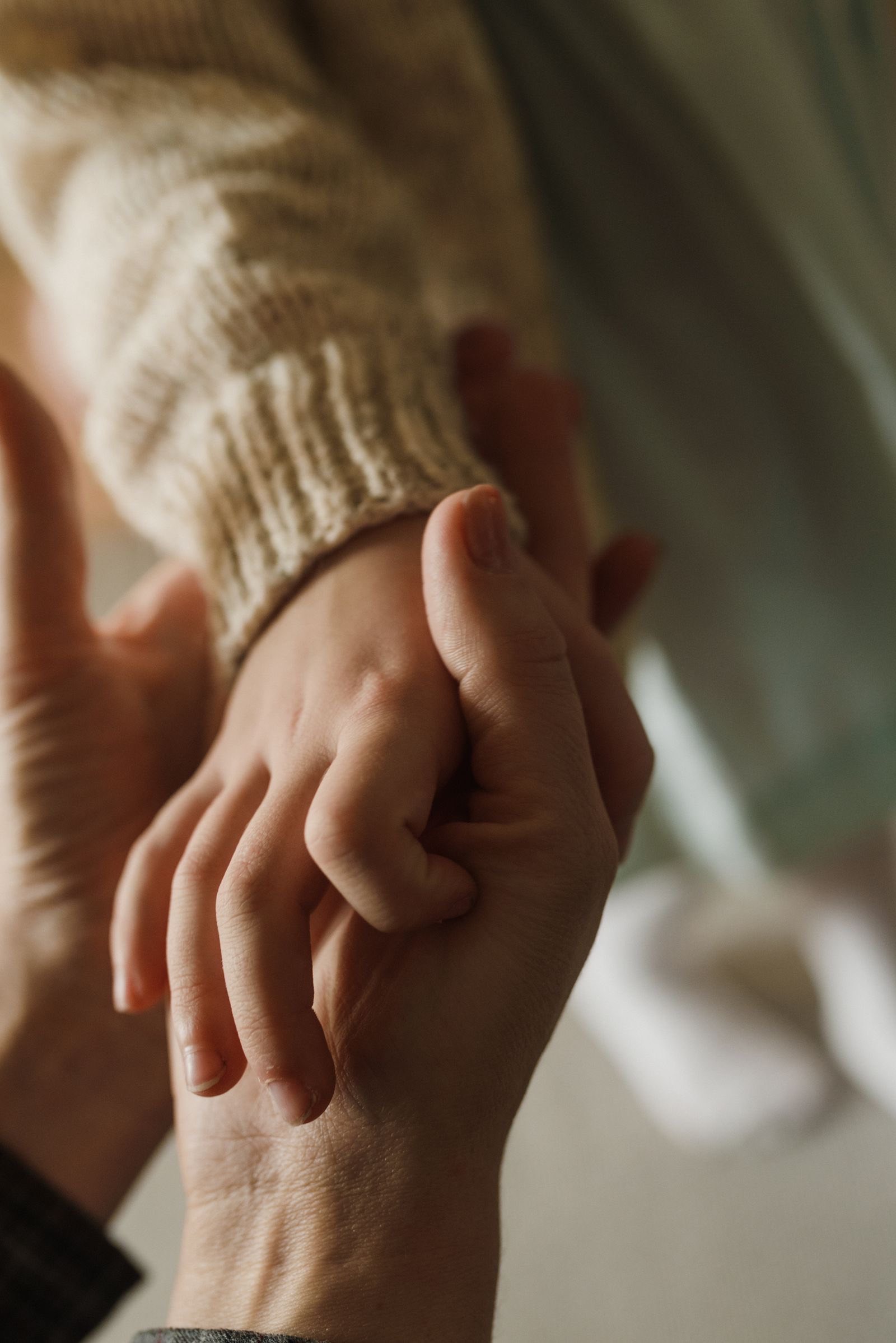 An adult's hands gently holding a child's hand
